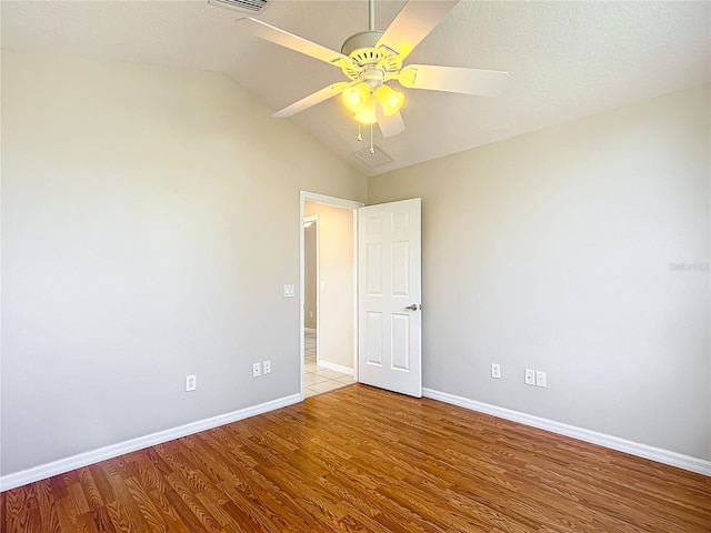 empty room featuring a ceiling fan, lofted ceiling, baseboards, and light wood-type flooring