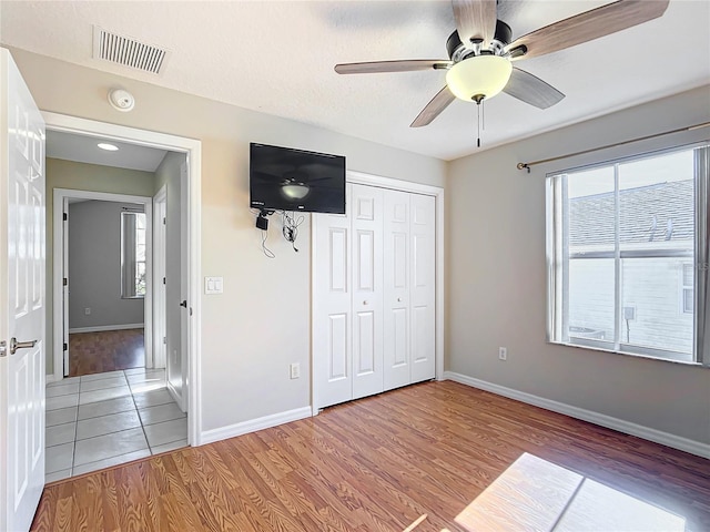 unfurnished bedroom featuring baseboards, visible vents, light wood-style flooring, ceiling fan, and a closet