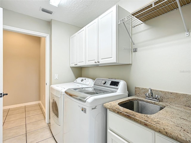 clothes washing area with light tile patterned floors, visible vents, washing machine and clothes dryer, cabinet space, and a sink