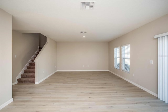 spare room featuring light wood-type flooring, visible vents, baseboards, and stairs