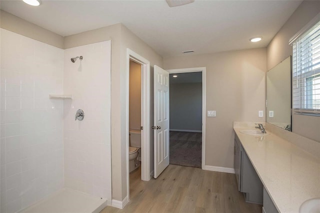 full bathroom with visible vents, tiled shower, toilet, wood finished floors, and vanity