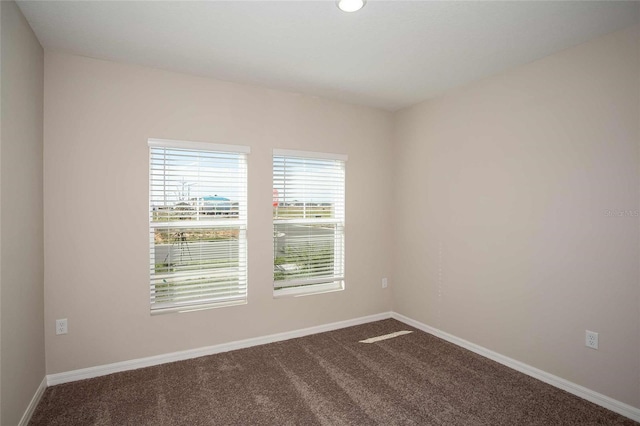 spare room featuring baseboards and dark carpet