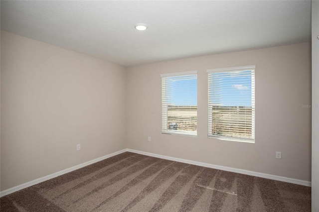 spare room featuring baseboards and dark colored carpet