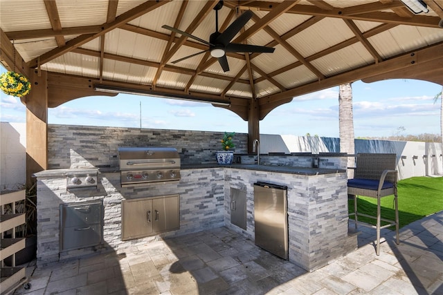 view of patio with grilling area, fence, a gazebo, an outdoor kitchen, and a sink