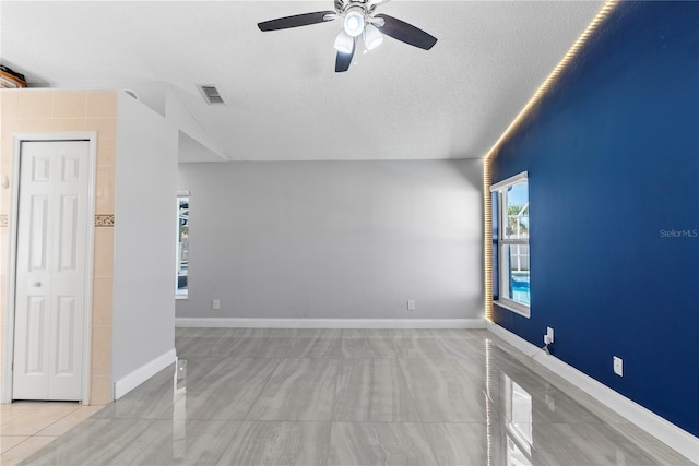 empty room with visible vents, ceiling fan, a textured ceiling, and baseboards