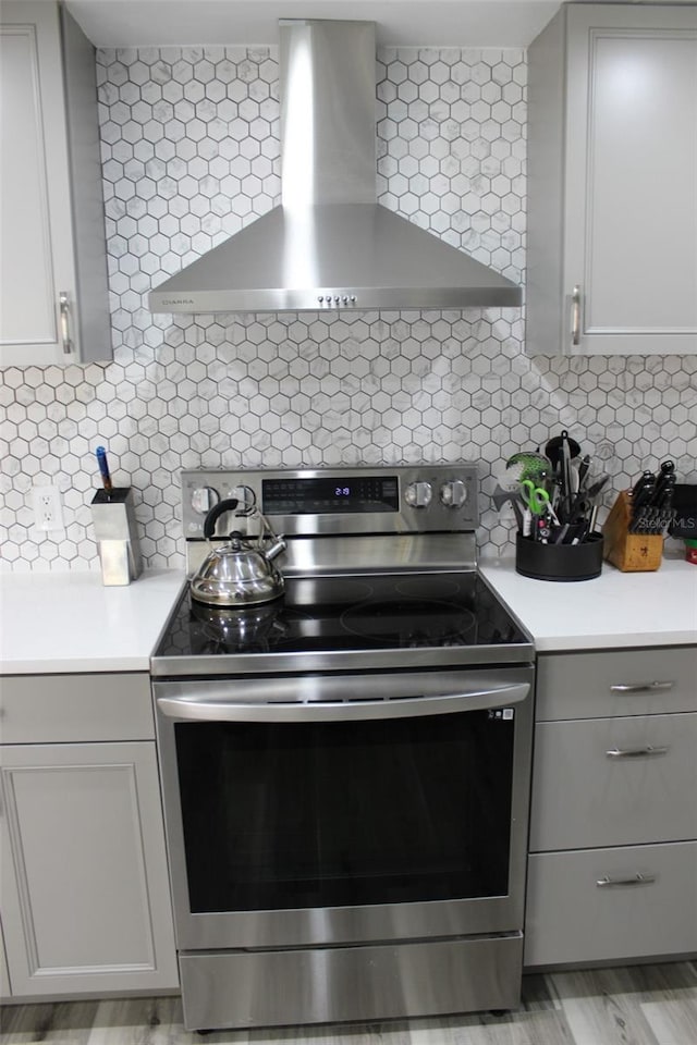 kitchen featuring electric range, light countertops, gray cabinets, wall chimney exhaust hood, and tasteful backsplash