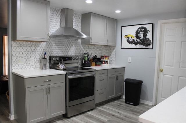 kitchen featuring wall chimney range hood, stainless steel electric stove, gray cabinets, and light countertops