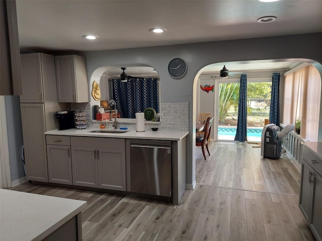 kitchen featuring arched walkways, light countertops, gray cabinetry, stainless steel dishwasher, and a sink