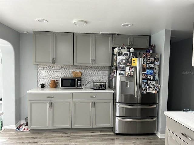 kitchen featuring arched walkways, light countertops, appliances with stainless steel finishes, gray cabinets, and tasteful backsplash