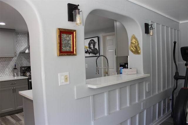 interior space featuring arched walkways, electric range, wood finished floors, wall chimney exhaust hood, and tasteful backsplash