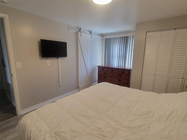 bedroom with a barn door, baseboards, a closet, and wood finished floors