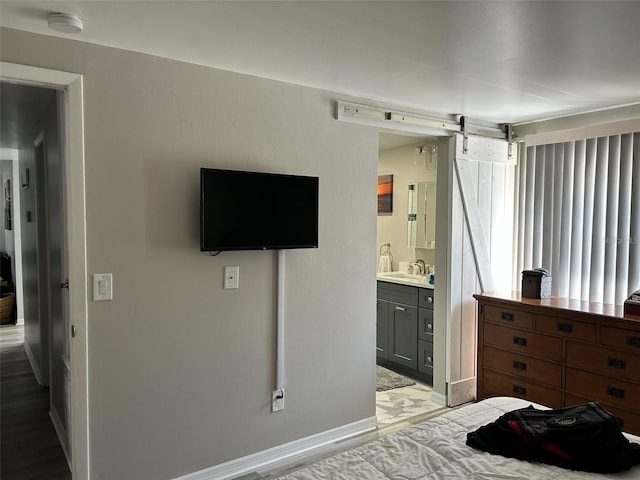 bedroom featuring a barn door, baseboards, ensuite bath, marble finish floor, and a sink