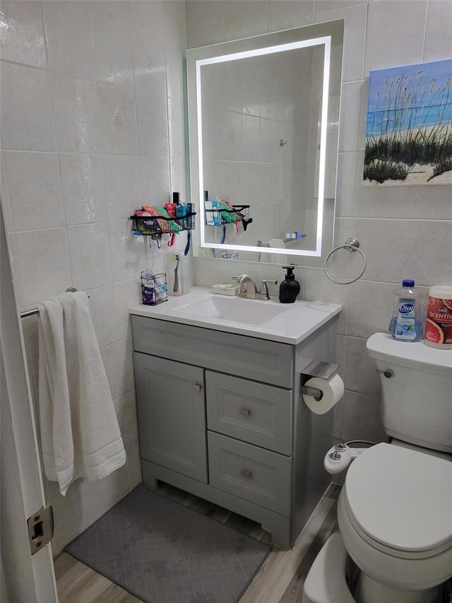 bathroom featuring toilet, wood finished floors, tile walls, and vanity