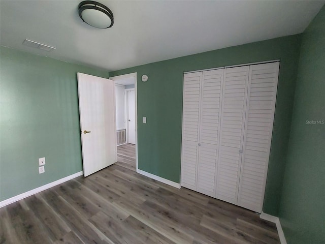 unfurnished bedroom featuring baseboards, a closet, visible vents, and wood finished floors