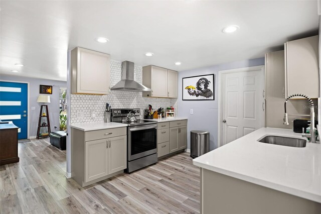 kitchen with gray cabinetry, a sink, wall chimney range hood, stainless steel electric range, and light countertops
