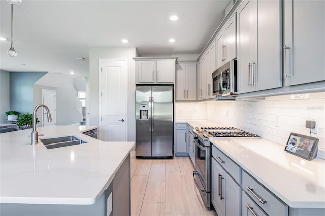 kitchen featuring stainless steel appliances, backsplash, a sink, and gray cabinetry