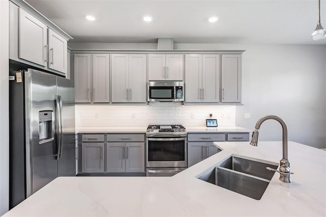 kitchen featuring appliances with stainless steel finishes, a sink, backsplash, and gray cabinetry