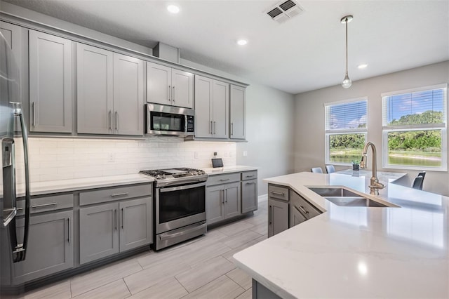 kitchen with visible vents, decorative backsplash, appliances with stainless steel finishes, gray cabinetry, and a sink