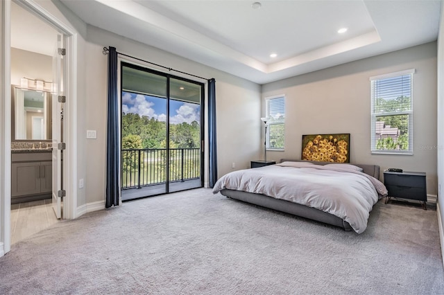 bedroom with carpet, a tray ceiling, recessed lighting, connected bathroom, and access to outside