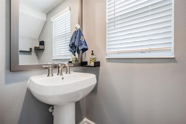 bathroom with vaulted ceiling, a sink, and a textured wall