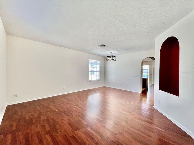 spare room featuring arched walkways, a textured ceiling, baseboards, and wood finished floors