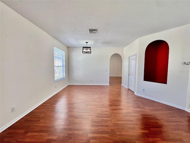 unfurnished room featuring a textured ceiling, arched walkways, wood finished floors, visible vents, and baseboards