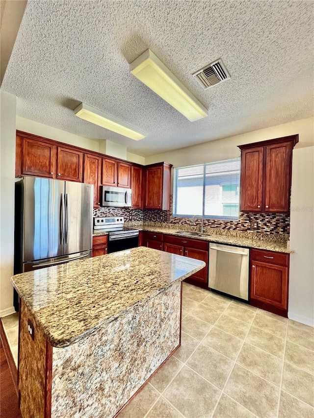 kitchen featuring visible vents, backsplash, appliances with stainless steel finishes, a sink, and a kitchen island