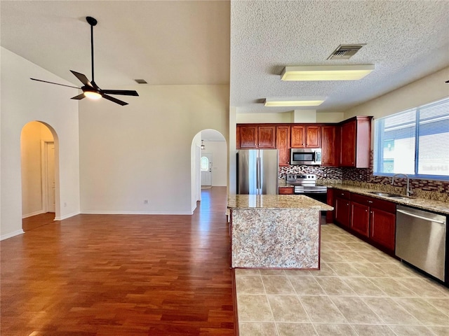 kitchen with arched walkways, tasteful backsplash, visible vents, appliances with stainless steel finishes, and a sink