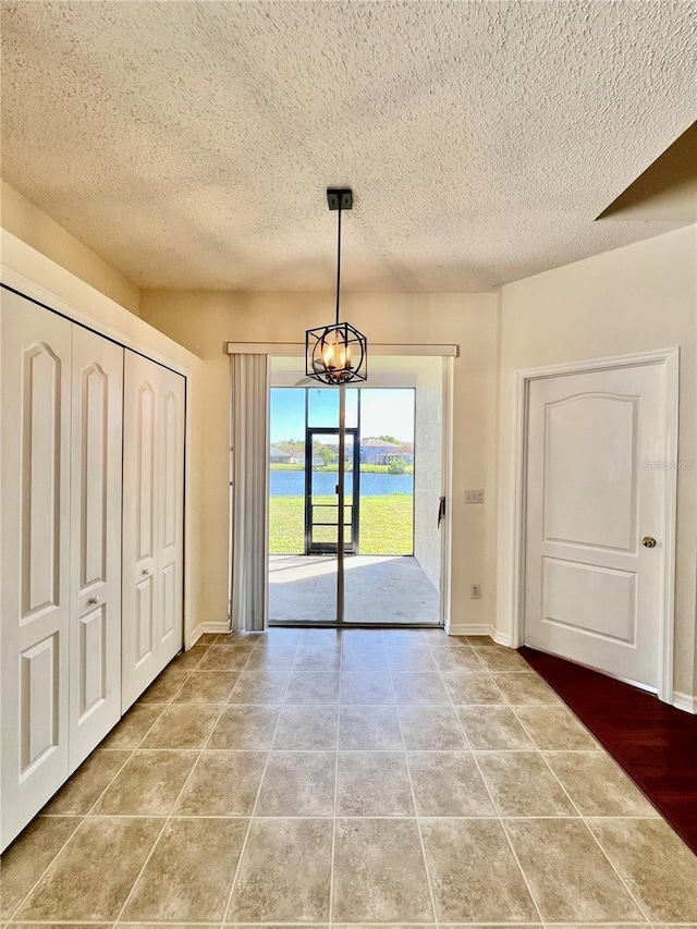 doorway with a notable chandelier, a textured ceiling, baseboards, and tile patterned floors