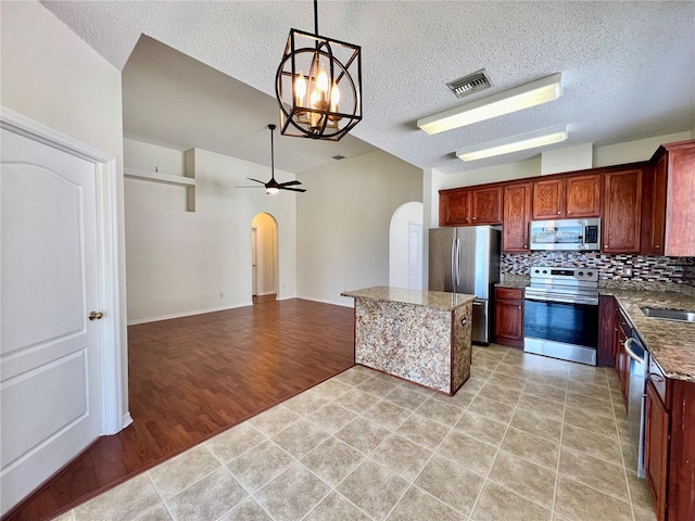 kitchen featuring arched walkways, visible vents, appliances with stainless steel finishes, decorative backsplash, and decorative light fixtures