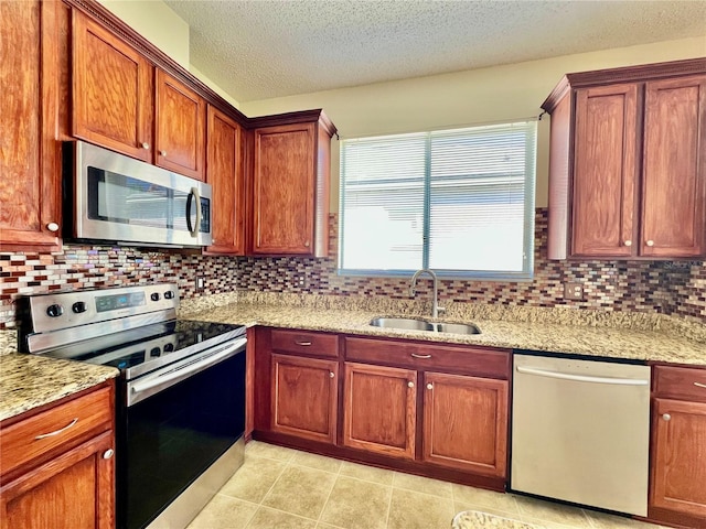 kitchen featuring light stone countertops, decorative backsplash, stainless steel appliances, and a sink