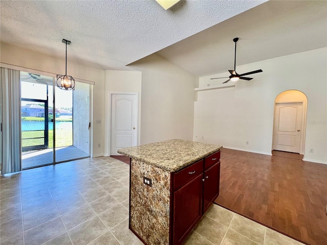 kitchen with arched walkways, a center island, a textured ceiling, pendant lighting, and ceiling fan with notable chandelier