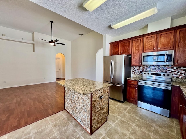 kitchen with stainless steel appliances, arched walkways, light stone counters, and a ceiling fan