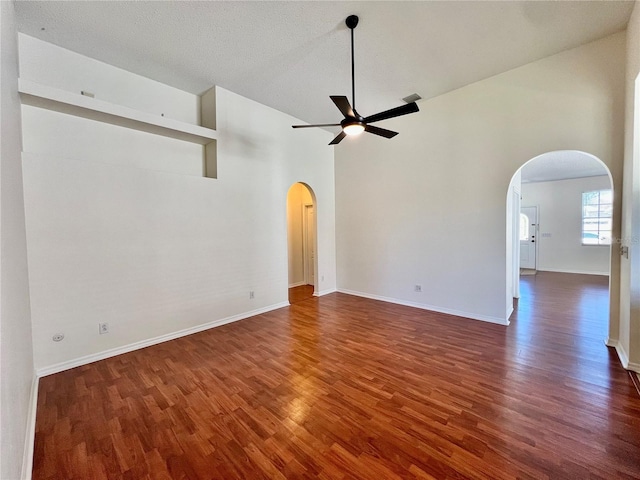 empty room with arched walkways, wood finished floors, a ceiling fan, and baseboards