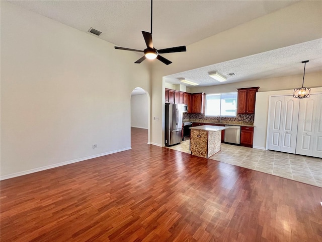 kitchen with arched walkways, stainless steel appliances, backsplash, open floor plan, and ceiling fan with notable chandelier