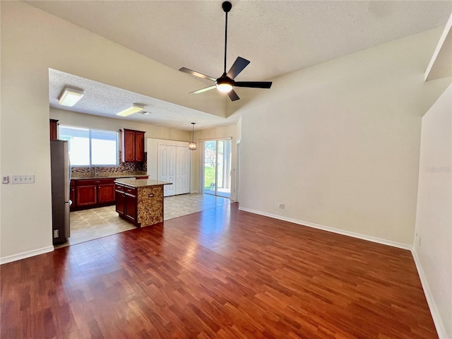 unfurnished living room featuring a textured ceiling, dark wood-style flooring, a wealth of natural light, and baseboards