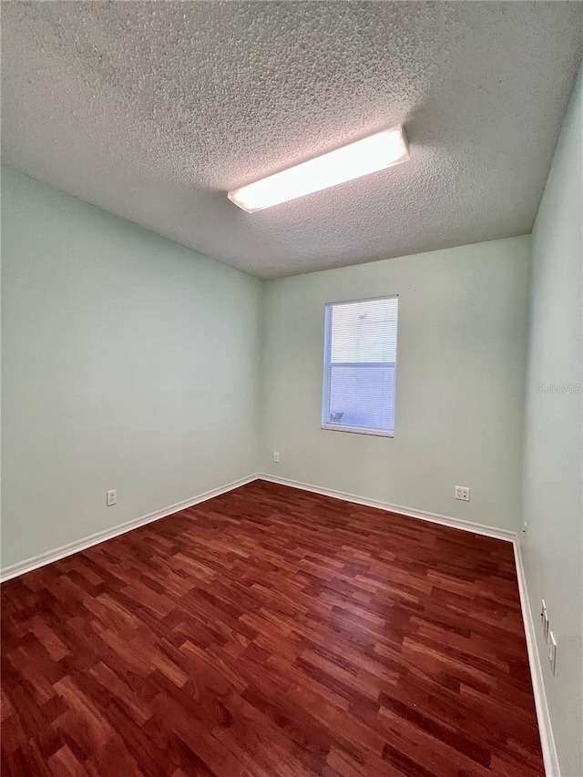 spare room with a textured ceiling, wood finished floors, and baseboards