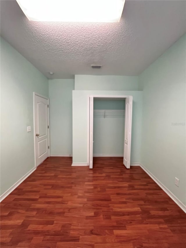 unfurnished bedroom with a textured ceiling, wood finished floors, visible vents, baseboards, and a closet