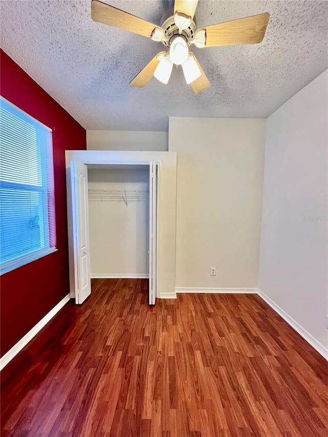 unfurnished bedroom with a closet, a textured ceiling, baseboards, and wood finished floors