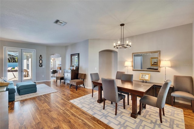 dining room with arched walkways, visible vents, baseboards, and wood finished floors