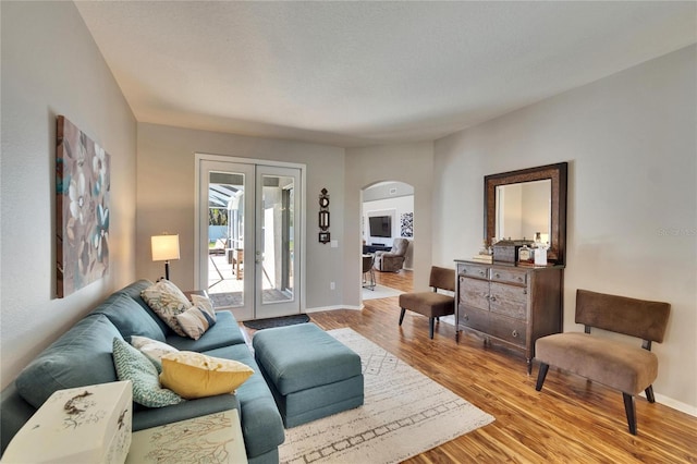 living area featuring baseboards, arched walkways, wood finished floors, and french doors