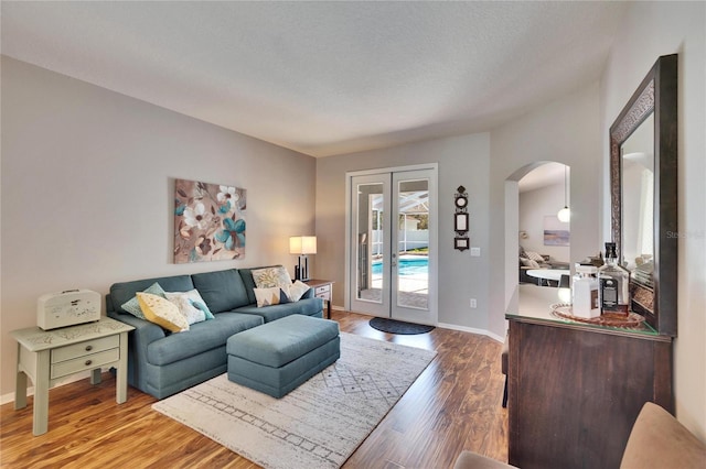 living room with a textured ceiling, wood finished floors, french doors, arched walkways, and baseboards