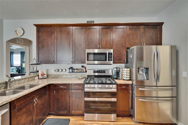 kitchen featuring light stone countertops, visible vents, arched walkways, a sink, and appliances with stainless steel finishes