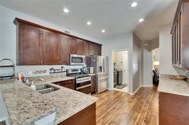 kitchen featuring light stone countertops, visible vents, arched walkways, a sink, and stainless steel appliances