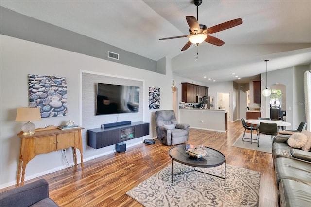 living room featuring visible vents, light wood-style floors, baseboards, ceiling fan, and vaulted ceiling