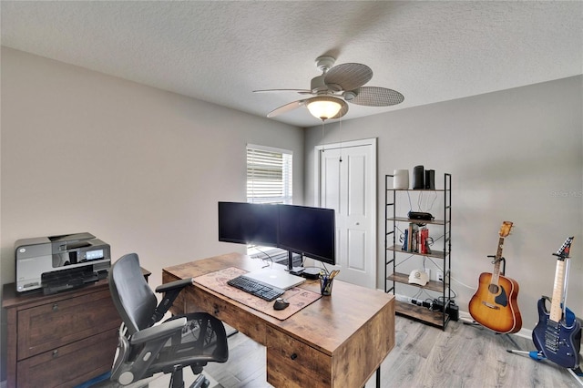 home office with baseboards, a ceiling fan, light wood-style floors, and a textured ceiling