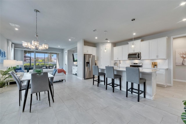 kitchen featuring visible vents, an island with sink, appliances with stainless steel finishes, open floor plan, and light countertops