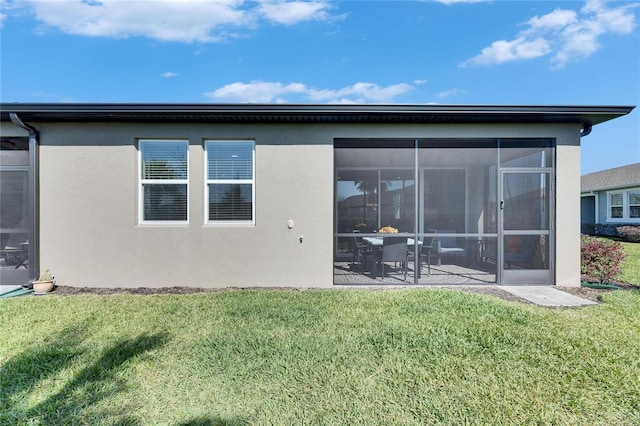 back of property with a lawn, a sunroom, and stucco siding