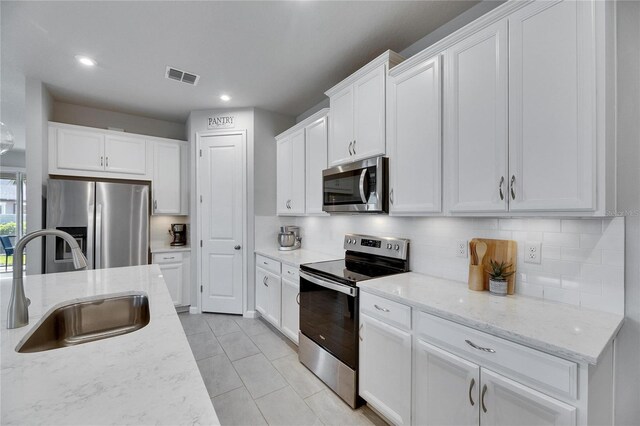 3753 Maxwell Park Dr, Sun City Center, FL 33573 - kitchen with stainless steel appliances, a sink, tasteful backsplash, white cabinetry, and light stone countertops