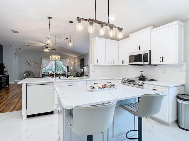 kitchen featuring stainless steel appliances, a peninsula, a kitchen island, a sink, and white cabinets